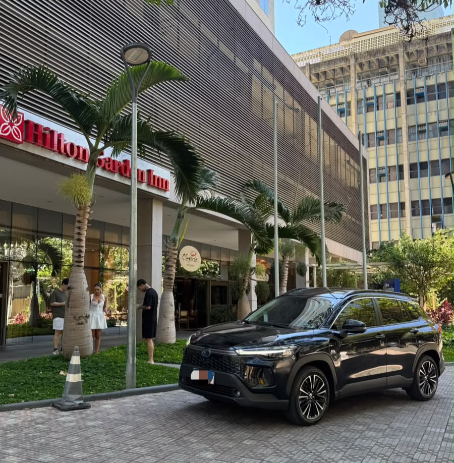 SUV preta estacionada em frente a um hotel com palmeiras