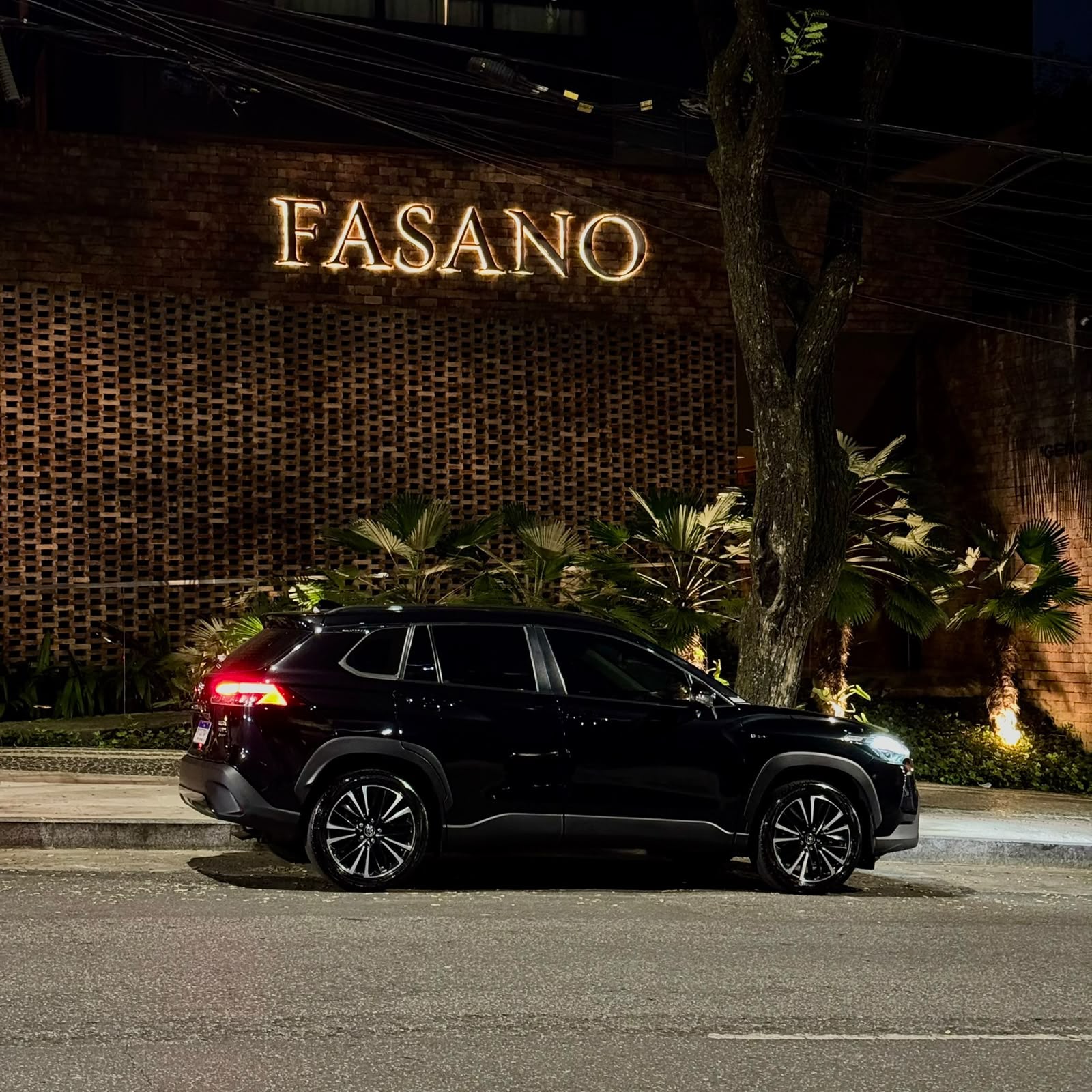 SUV preta da Santiago estacionada à noite em frente à fachada de tijolos do restaurante Fasano